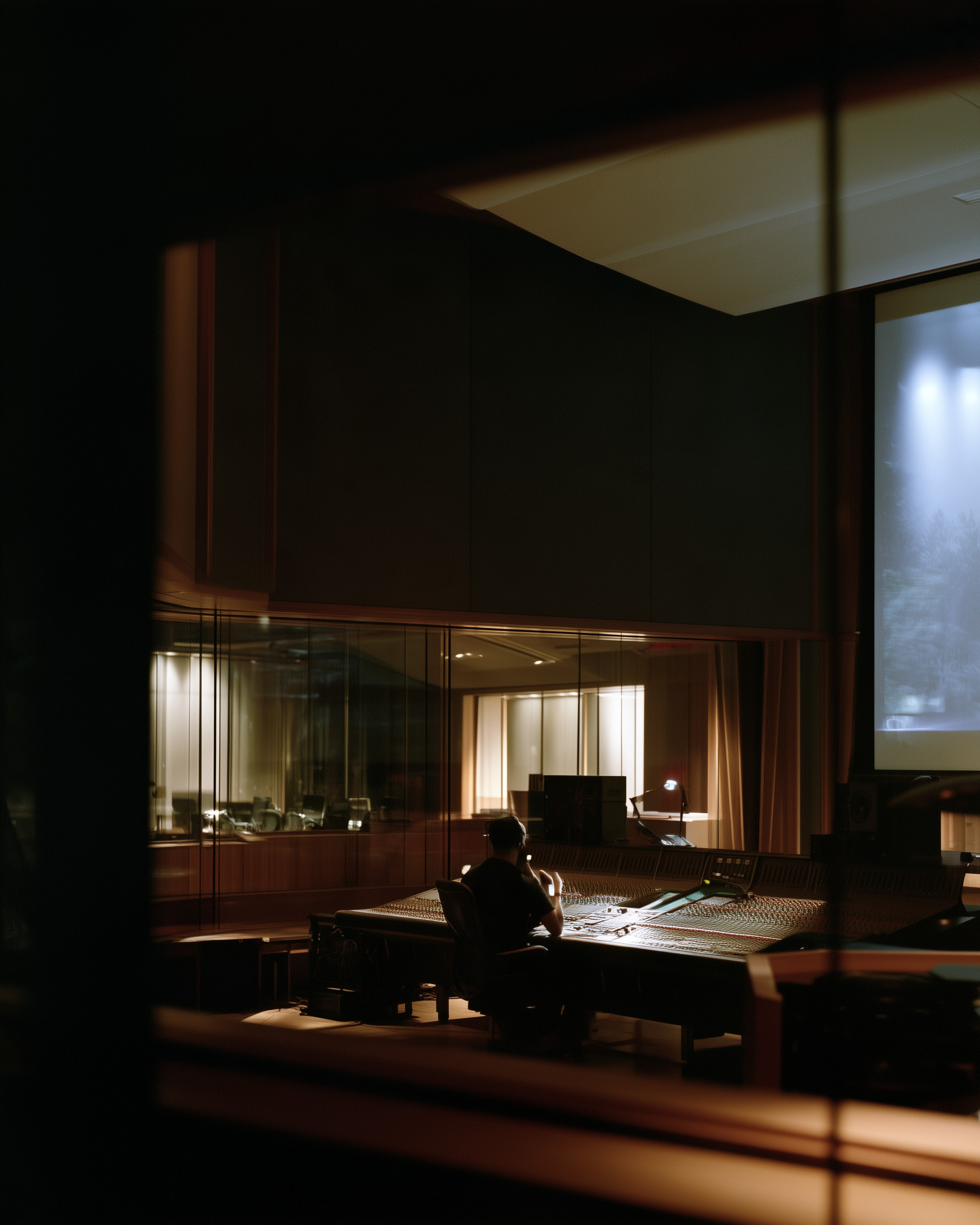 An engineer at a mixing console in a dark studio, a screen glowing above