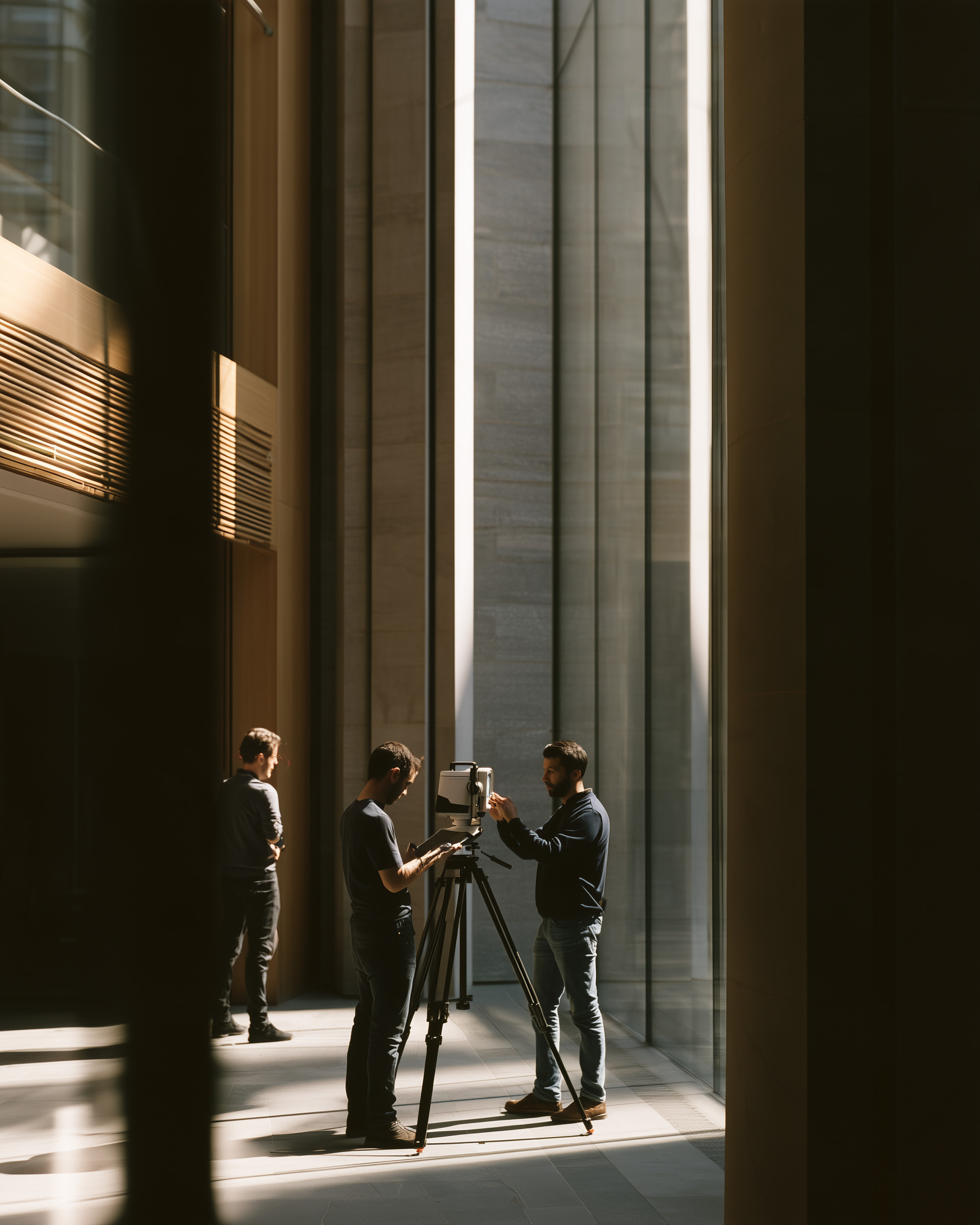 Three people setting up a laser scanner on a tripod in a sunlit stone atrium